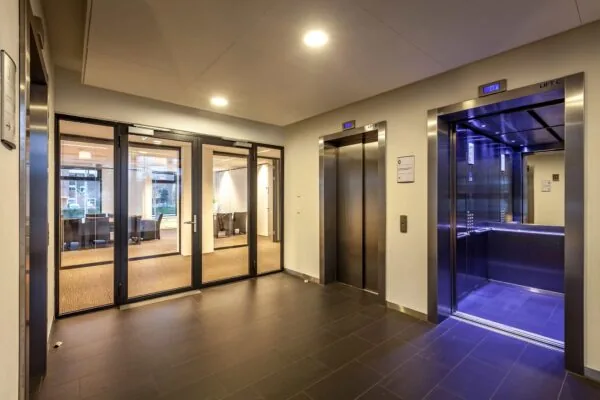 Moderne liftlobby met drie liften en glazen deuren naar een kantoorruimte aan de Prinses Beatrixlaan.